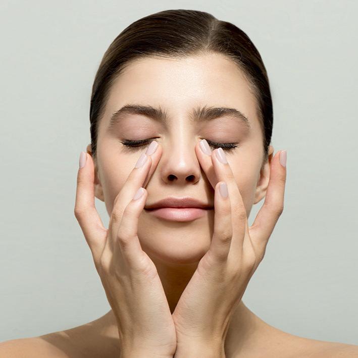 woman massaging her eyes against grey background